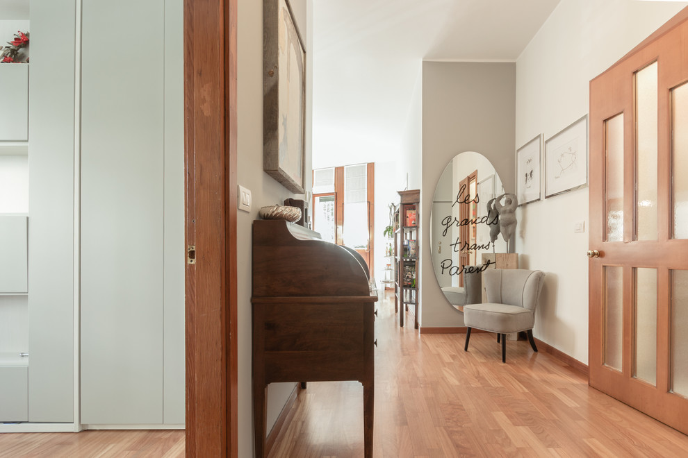 This is an example of a mid-sized contemporary foyer in Milan with grey walls, medium hardwood floors, a single front door and a white front door.