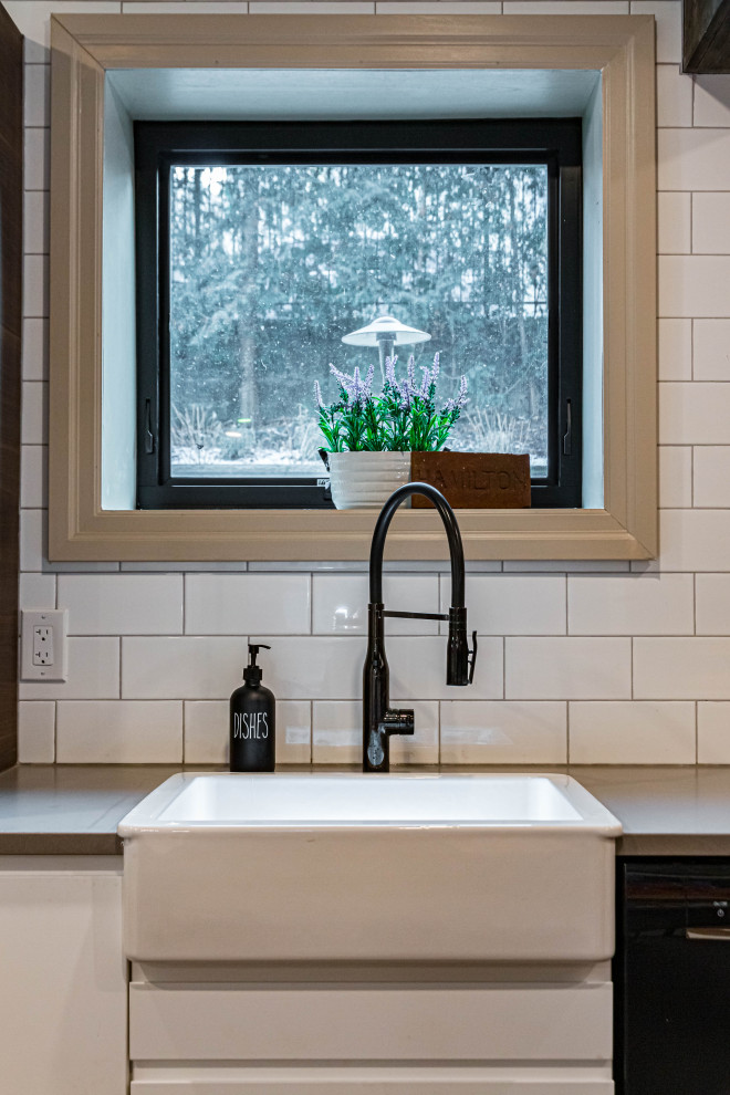 Example of a mid-sized mountain style u-shaped ceramic tile, black floor and exposed beam eat-in kitchen design in Toronto with a farmhouse sink, flat-panel cabinets, white cabinets, quartz countertops, white backsplash, subway tile backsplash, stainless steel appliances, an island and gray countertops