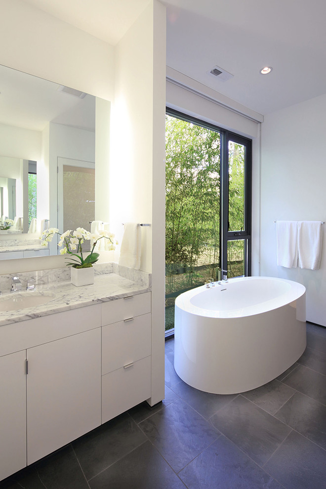 This is an example of a contemporary bathroom in Raleigh with an undermount sink, flat-panel cabinets, white cabinets, a freestanding tub, white tile and white walls.