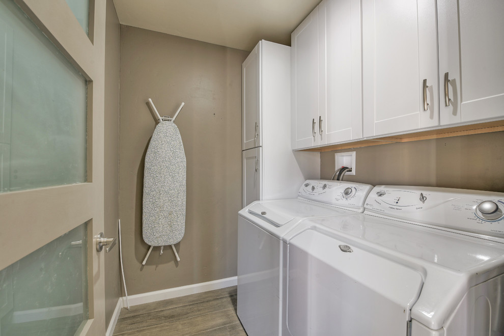 Small contemporary galley dedicated laundry room in San Diego with shaker cabinets, white cabinets, grey walls, light hardwood floors, a side-by-side washer and dryer and grey floor.