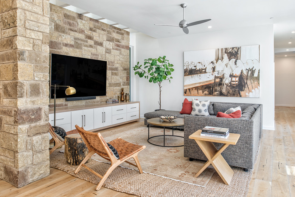 Eclectic formal open concept living room in Austin with white walls, light hardwood floors, a wall-mounted tv and brown floor.