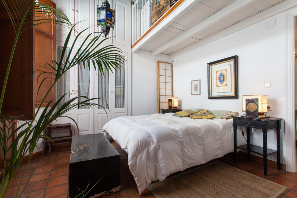 Design ideas for a mid-sized tropical bedroom in Seville with white walls, terra-cotta floors and no fireplace.