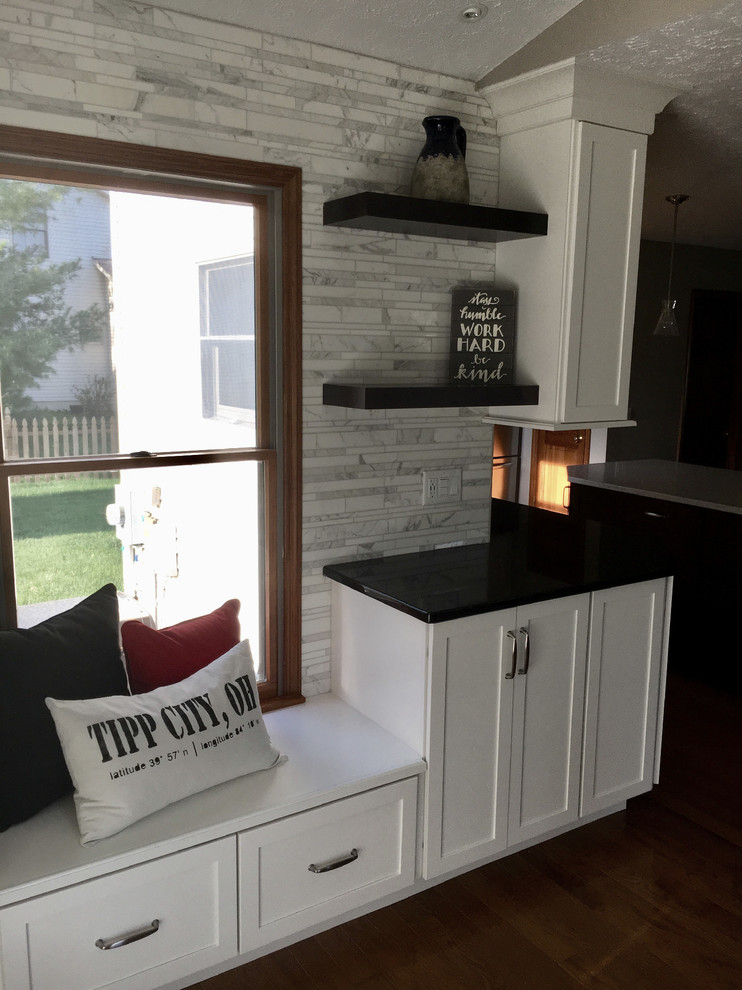 Inspiration for a large transitional single-wall medium tone wood floor eat-in kitchen remodel with an undermount sink, shaker cabinets, white cabinets, granite countertops, multicolored backsplash, marble backsplash, stainless steel appliances, an island and black countertops