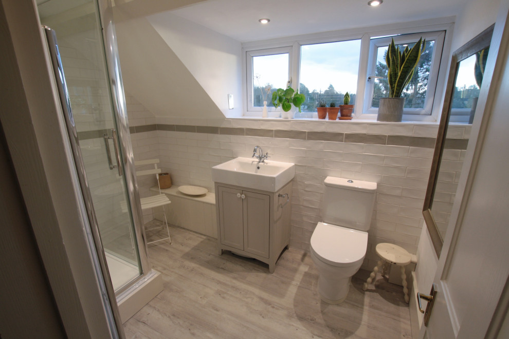 This is an example of a small vintage ensuite bathroom in Oxfordshire with shaker cabinets, light wood cabinets, a corner shower, a two-piece toilet, white tiles, ceramic tiles, white walls, vinyl flooring, a trough sink, white floors, a hinged door, a single sink and a freestanding vanity unit.