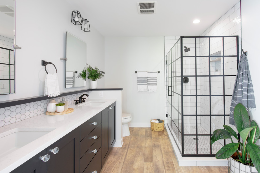 Photo of a mid-sized contemporary master bathroom in Milwaukee with black cabinets, a corner shower, a two-piece toilet, white tile, subway tile, vinyl floors, an undermount sink, engineered quartz benchtops, brown floor, a hinged shower door, white benchtops, a niche, a double vanity, a built-in vanity, grey walls and shaker cabinets.