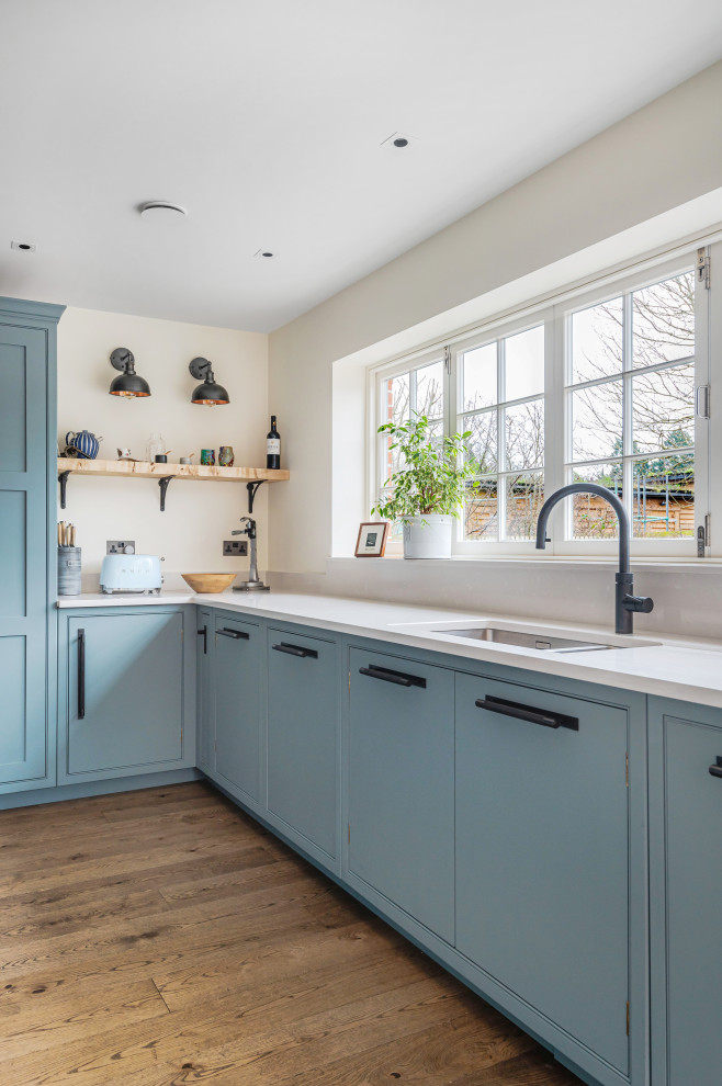 Large industrial l-shaped eat-in kitchen in Berkshire with a drop-in sink, shaker cabinets, blue cabinets, wood benchtops, panelled appliances, with island and white benchtop.