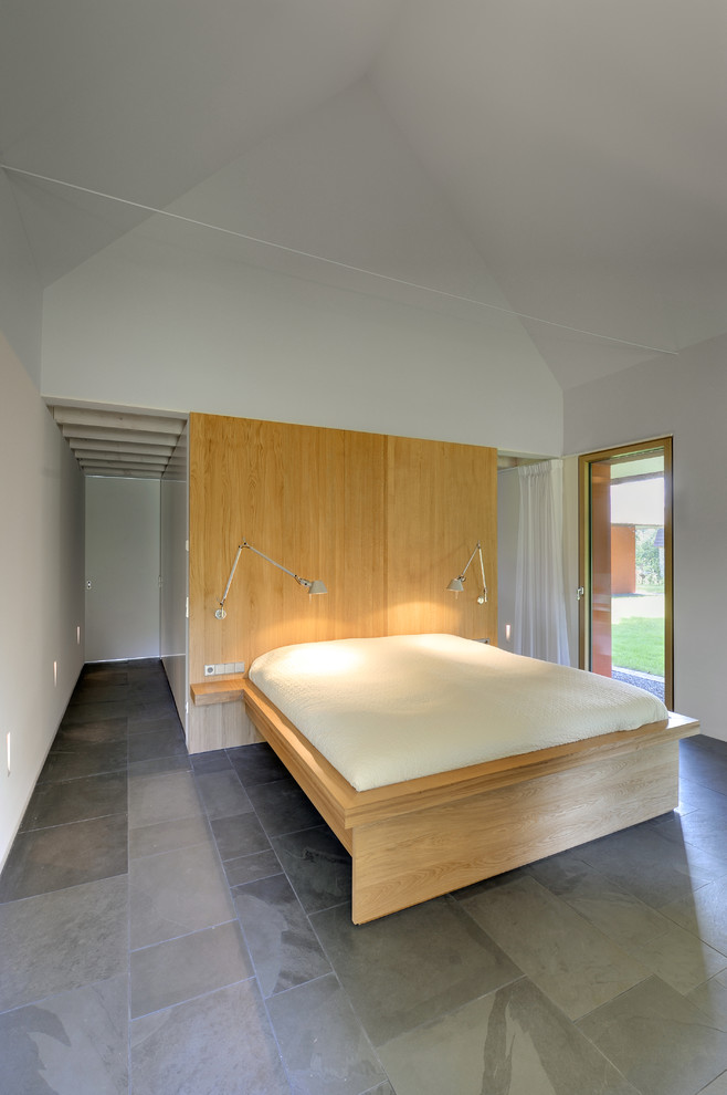 This is an example of a contemporary bedroom in Berlin with white walls, slate floors and no fireplace.