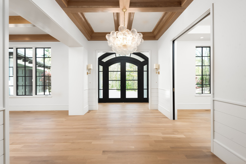 Example of a mid-sized transitional light wood floor, coffered ceiling and shiplap wall entry hall design with white walls and a black front door