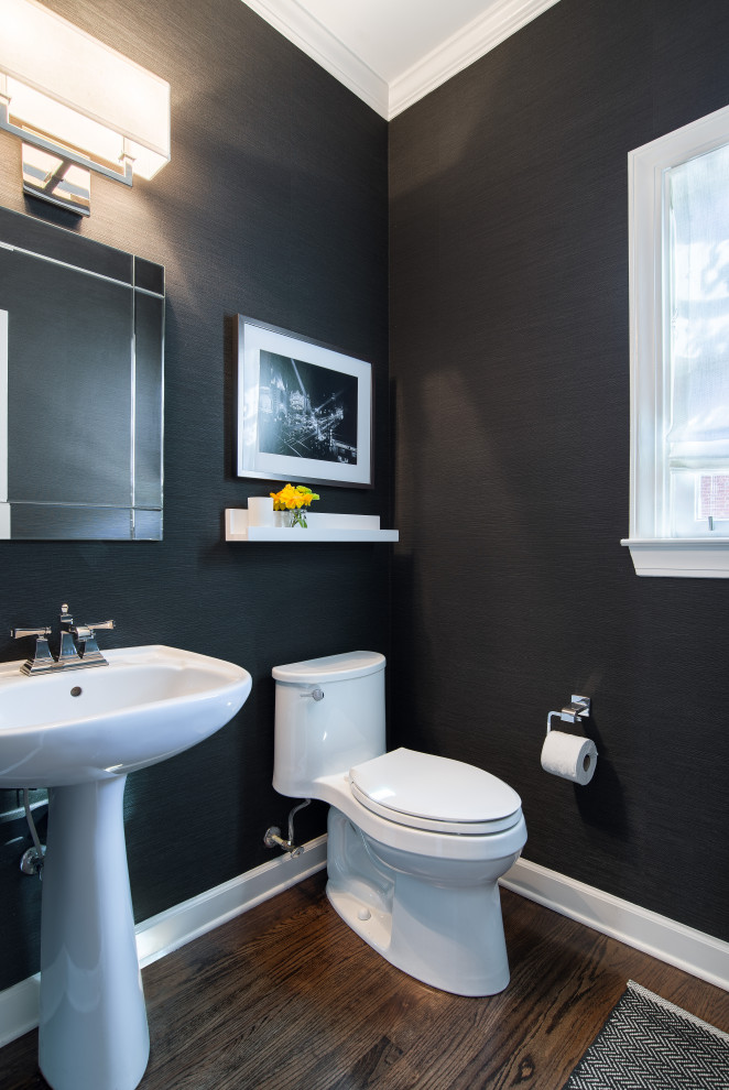 This is an example of a small transitional powder room in Atlanta with a one-piece toilet, black walls, dark hardwood floors, a pedestal sink and wallpaper.