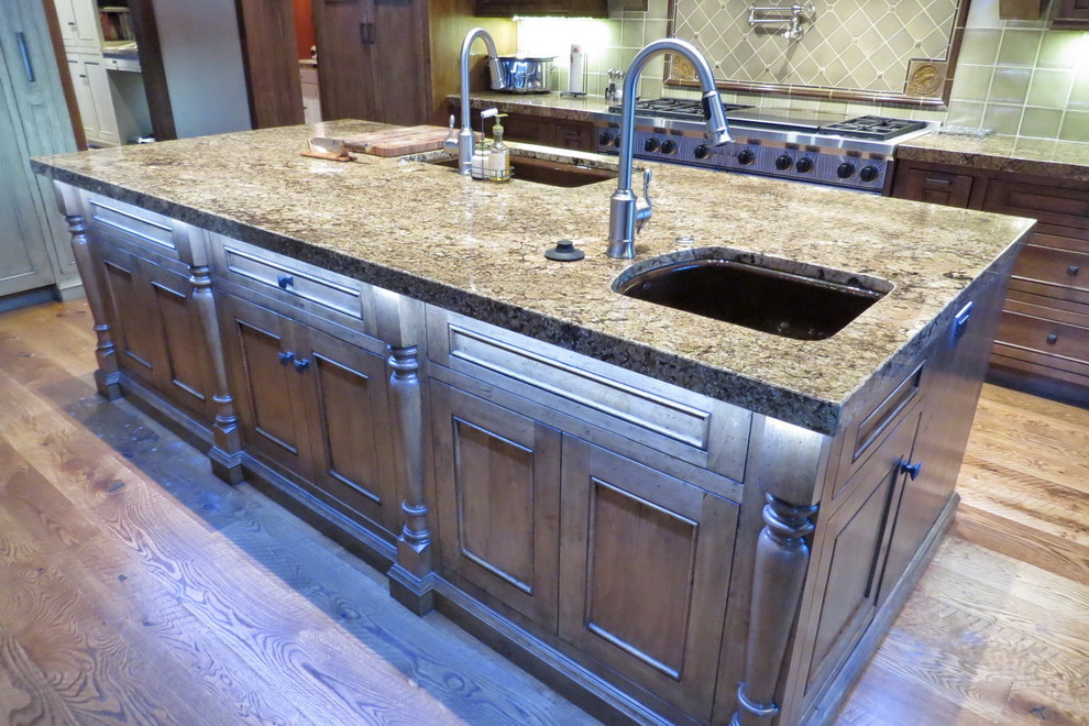 Photo of a large country u-shaped eat-in kitchen in Other with an undermount sink, raised-panel cabinets, medium wood cabinets, granite benchtops, stone tile splashback, panelled appliances, medium hardwood floors and multiple islands.
