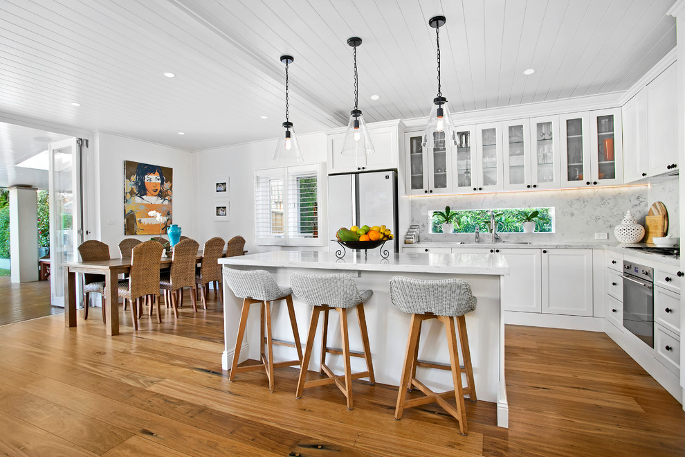 Photo of a mid-sized transitional l-shaped open plan kitchen in Sydney with white cabinets, marble benchtops, multi-coloured splashback, marble splashback, medium hardwood floors, multiple islands, brown floor, white benchtop, stainless steel appliances, a drop-in sink and shaker cabinets.