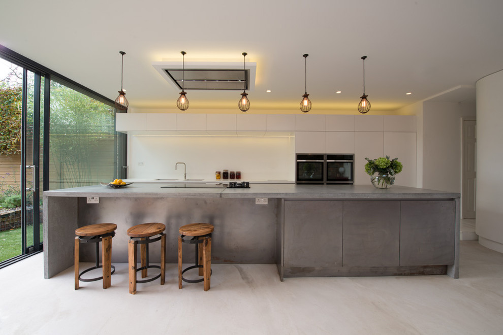 Design ideas for a mid-sized modern galley open plan kitchen in London with concrete benchtops, white floor, flat-panel cabinets, grey cabinets, white splashback, black appliances and with island.