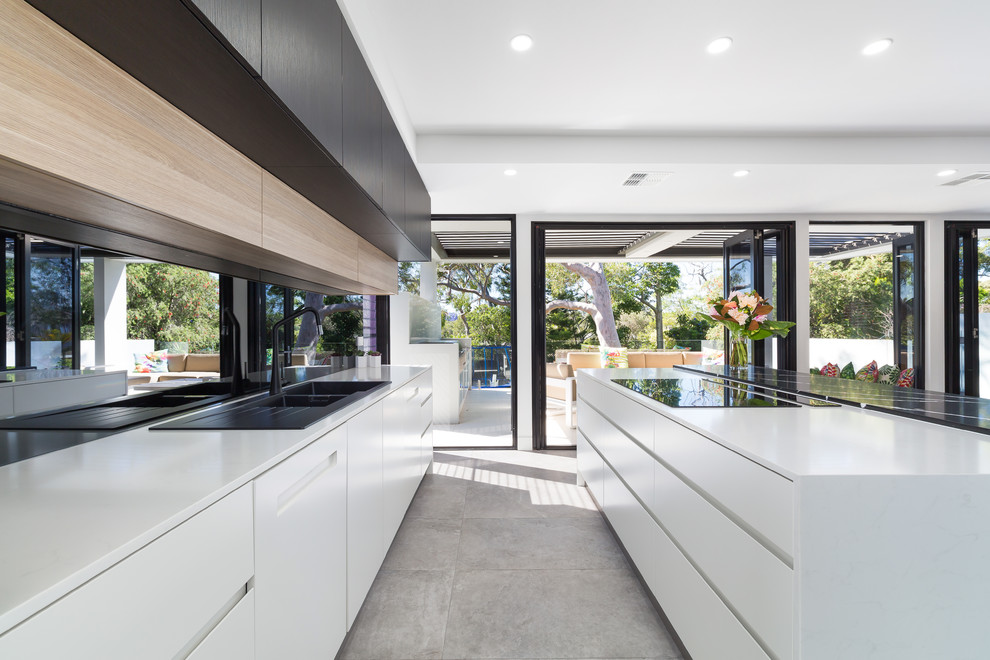 This is an example of a large contemporary galley open plan kitchen in Sydney with a double-bowl sink, white cabinets, black appliances, porcelain floors, with island, grey floor and white benchtop.