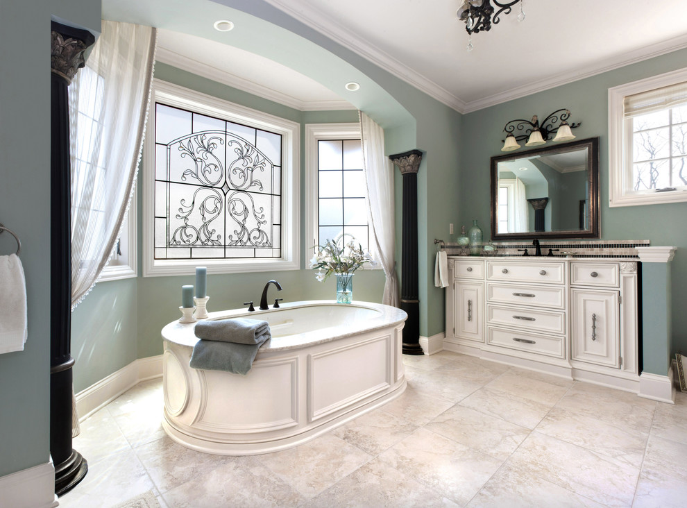 Photo of a large traditional master bathroom in Milwaukee with white cabinets, beige tile, an undermount sink, recessed-panel cabinets, a freestanding tub, a one-piece toilet, green walls and travertine floors.