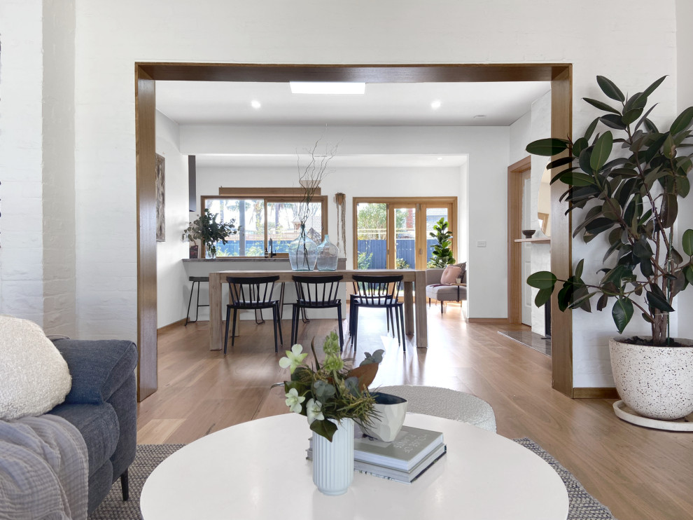 Idee per una sala da pranzo aperta verso il soggiorno minimalista con pareti bianche, pavimento in legno massello medio e cornice del camino in mattoni