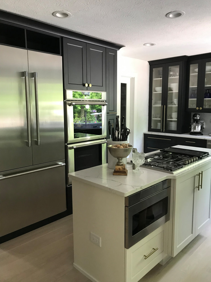 Photo of a mid-sized transitional u-shaped eat-in kitchen in Cleveland with an undermount sink, shaker cabinets, black cabinets, white splashback, marble splashback, stainless steel appliances, light hardwood floors, with island, white floor, white benchtop and quartz benchtops.