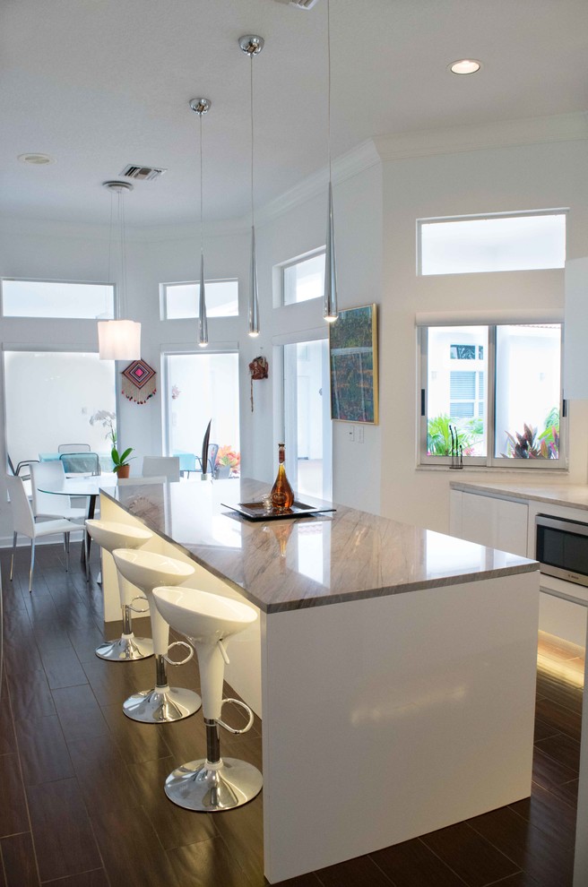 Mid-sized contemporary l-shaped eat-in kitchen in Miami with an integrated sink, flat-panel cabinets, white cabinets, granite benchtops, white splashback, stainless steel appliances, porcelain floors, with island, subway tile splashback and brown floor.