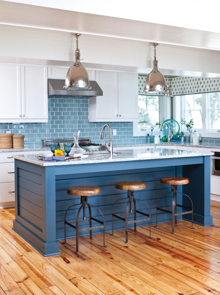 Design ideas for a beach style l-shaped kitchen in Other with an undermount sink, recessed-panel cabinets, white cabinets, blue splashback, subway tile splashback, stainless steel appliances, medium hardwood floors, with island, brown floor and grey benchtop.