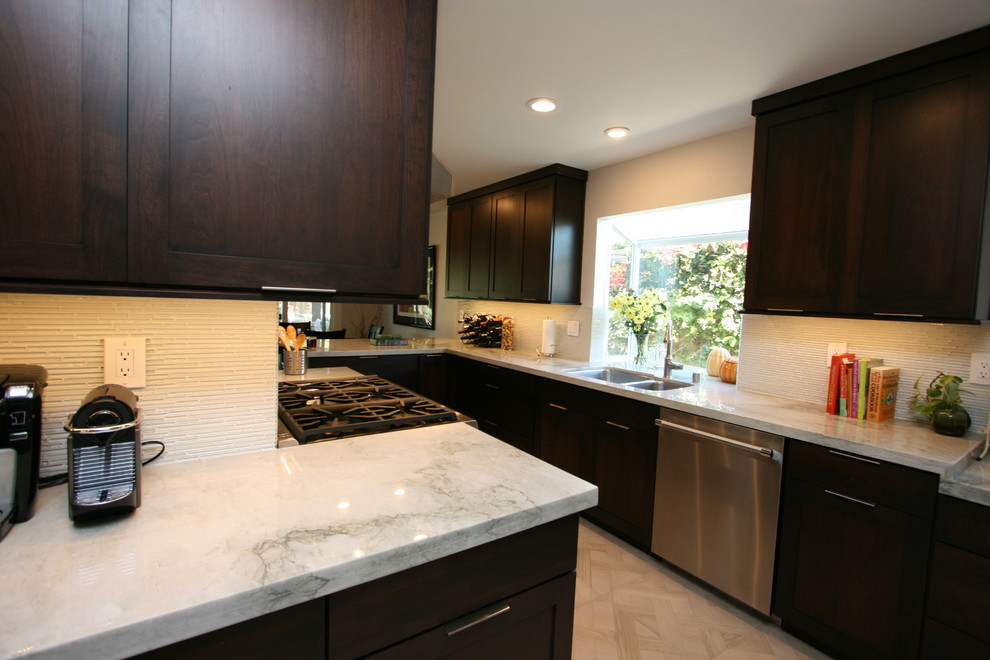 Mid-sized transitional l-shaped porcelain tile kitchen photo in Orange County with a double-bowl sink, recessed-panel cabinets, dark wood cabinets, quartzite countertops, white backsplash, glass tile backsplash, stainless steel appliances and no island
