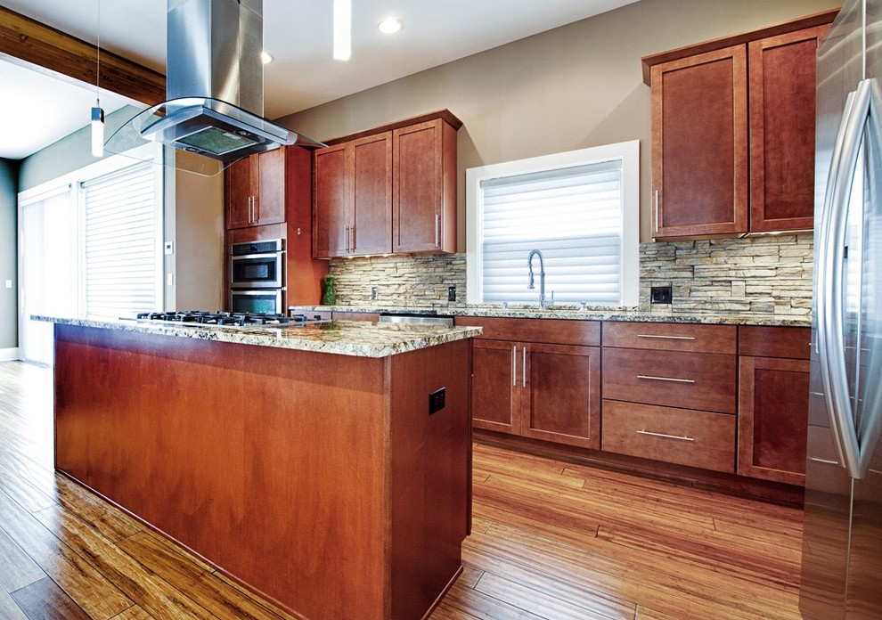 Large transitional l-shaped eat-in kitchen in Seattle with an undermount sink, raised-panel cabinets, brown cabinets, granite benchtops, grey splashback, slate splashback, stainless steel appliances, bamboo floors, brown floor and multiple islands.