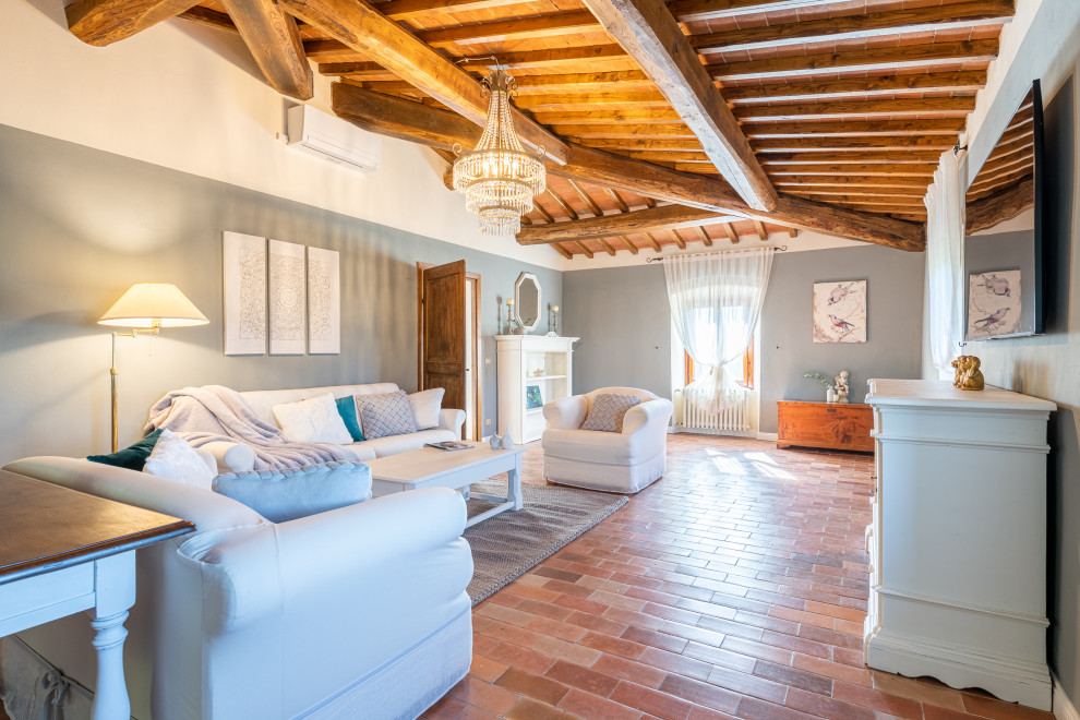 Photo of a large mediterranean open concept family room in Florence with a library, terra-cotta floors, a wall-mounted tv, orange floor, exposed beam and grey walls.
