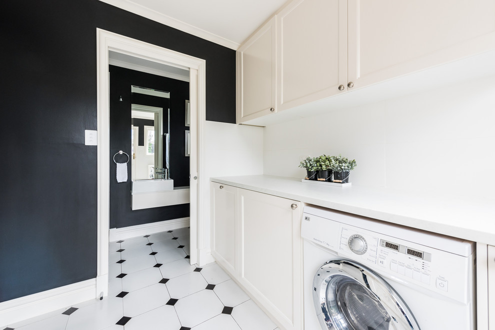 This is an example of a mid-sized contemporary single-wall dedicated laundry room in Melbourne with shaker cabinets, white cabinets, quartz benchtops, black walls, ceramic floors, a side-by-side washer and dryer, multi-coloured floor and white benchtop.