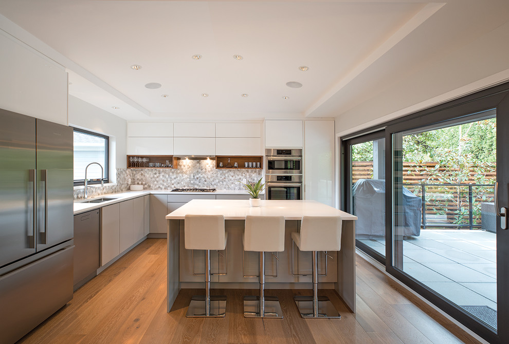 Photo of a mid-sized modern l-shaped eat-in kitchen in Vancouver with an undermount sink, flat-panel cabinets, white cabinets, granite benchtops, grey splashback, ceramic splashback, stainless steel appliances, medium hardwood floors, with island and white benchtop.
