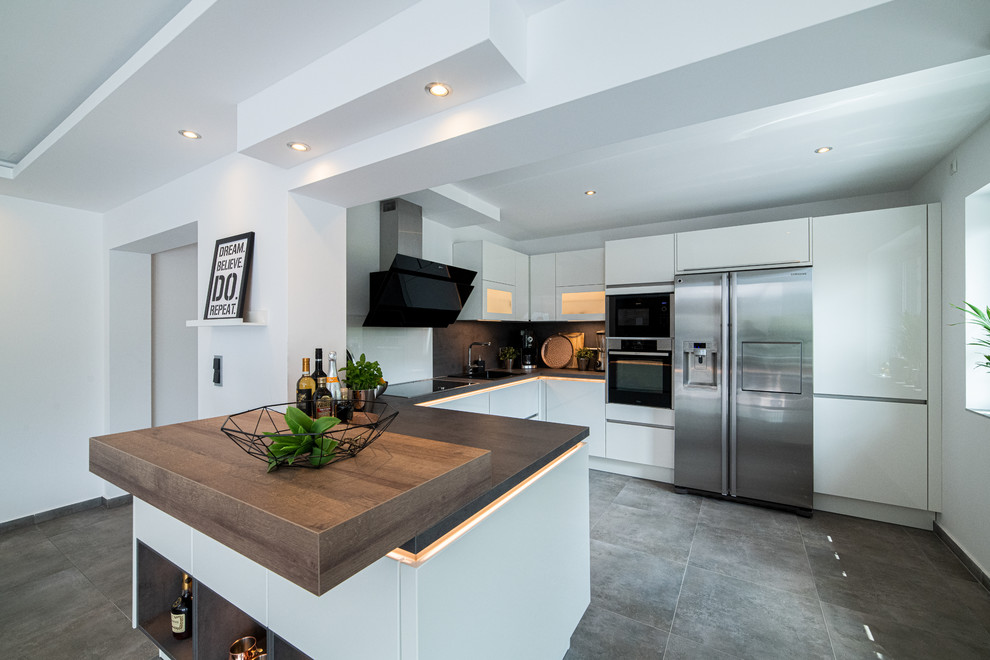 Design ideas for a mid-sized contemporary u-shaped kitchen in Hanover with ceramic floors, grey floor, a single-bowl sink, flat-panel cabinets, white cabinets, wood benchtops, brown splashback, timber splashback, stainless steel appliances, a peninsula and brown benchtop.