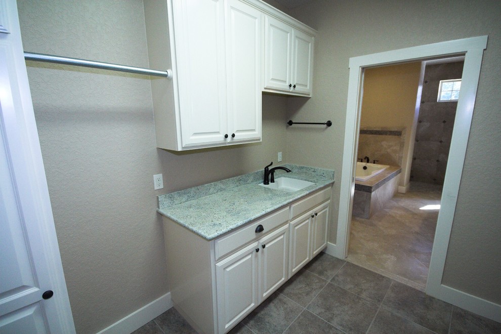 Inspiration for a mid-sized traditional single-wall dedicated laundry room in Austin with an undermount sink, raised-panel cabinets, white cabinets, granite benchtops, beige walls, porcelain floors, a side-by-side washer and dryer, grey floor and green benchtop.