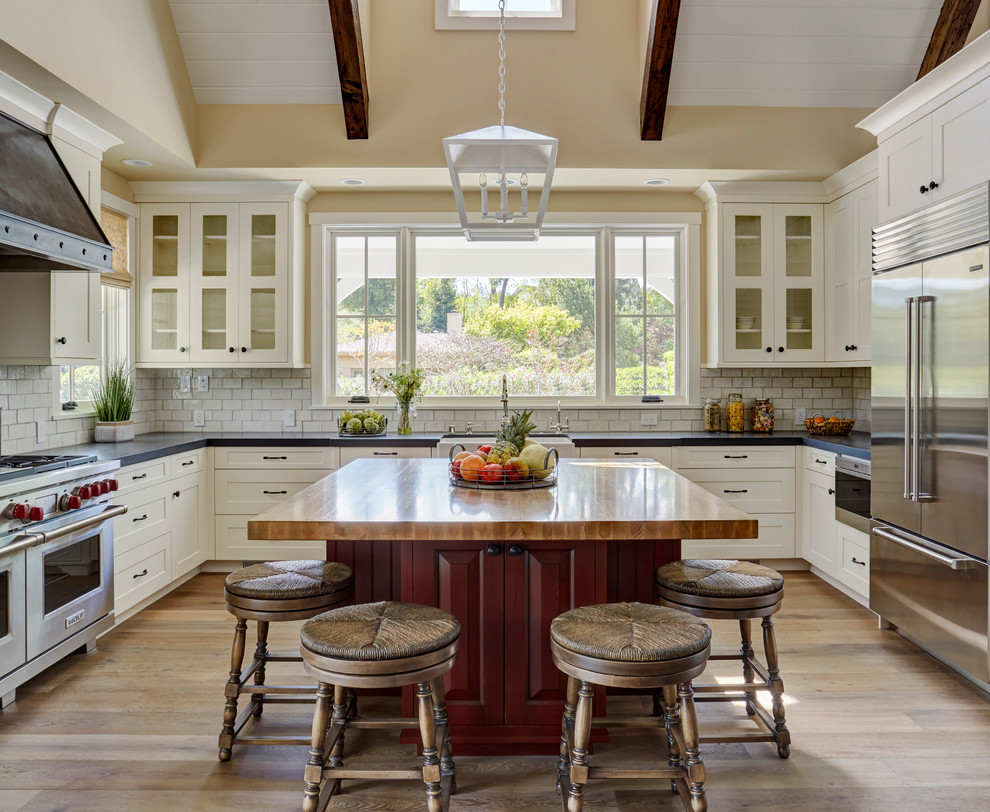 Design ideas for a mid-sized country u-shaped eat-in kitchen in San Francisco with a farmhouse sink, shaker cabinets, white cabinets, wood benchtops, white splashback, subway tile splashback, stainless steel appliances, medium hardwood floors, with island, brown floor and multi-coloured benchtop.