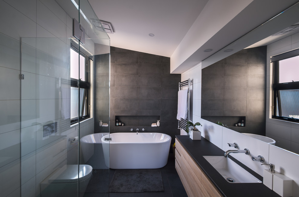 Design ideas for a mid-sized modern master bathroom in Melbourne with flat-panel cabinets, medium wood cabinets, a freestanding tub, a corner shower, a wall-mount toilet, gray tile, porcelain tile, white walls, porcelain floors, an undermount sink and engineered quartz benchtops.