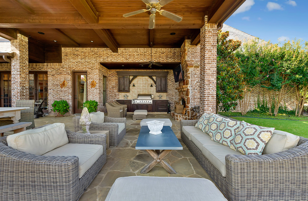 Photo of a traditional backyard patio in Dallas with an outdoor kitchen, natural stone pavers and a roof extension.