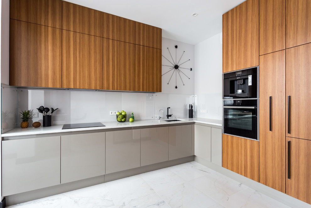 This is an example of a contemporary l-shaped kitchen in Saint Petersburg with an undermount sink, flat-panel cabinets, medium wood cabinets, white splashback, glass sheet splashback, black appliances, no island, white floor and white benchtop.