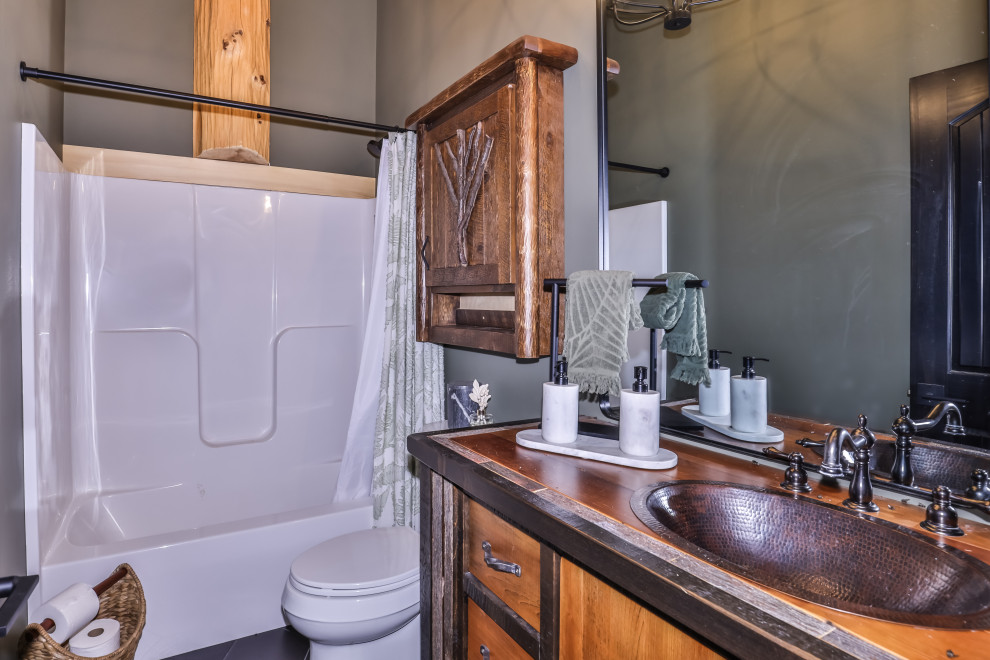 Alcove bathtub - small rustic ceramic tile, gray floor, single-sink and vaulted ceiling alcove bathtub idea with furniture-like cabinets, brown cabinets, a one-piece toilet, green walls, a drop-in sink, wood countertops and brown countertops