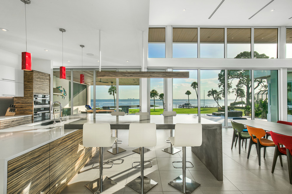 This is an example of a large modern l-shaped open plan kitchen in Tampa with an undermount sink, flat-panel cabinets, quartz benchtops, grey splashback, glass sheet splashback, stainless steel appliances, porcelain floors, with island, grey floor, white benchtop and white cabinets.