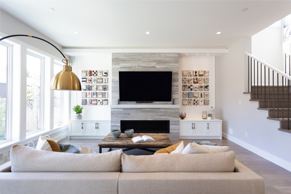 Inspiration for a large transitional open concept family room in Vancouver with white walls, a ribbon fireplace, a tile fireplace surround, a wall-mounted tv, light hardwood floors and beige floor.
