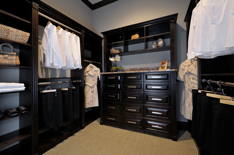 This is an example of a large transitional gender-neutral walk-in wardrobe in Miami with raised-panel cabinets, dark wood cabinets, carpet and beige floor.
