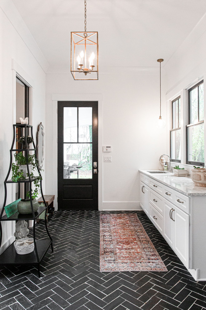 Mid-sized country galley dedicated laundry room in Atlanta with an undermount sink, shaker cabinets, white cabinets, granite benchtops, granite splashback, white walls, limestone floors, a side-by-side washer and dryer and black floor.