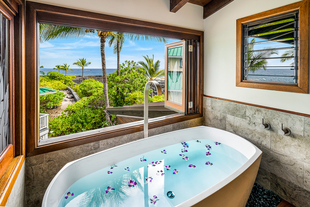 Inspiration for a mid-sized tropical master bathroom in Hawaii with flat-panel cabinets, medium wood cabinets, a freestanding tub, an alcove shower, a two-piece toilet, white tile, limestone, white walls, slate floors, an undermount sink, granite benchtops, black floor, a hinged shower door and black benchtops.