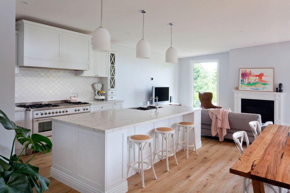 Inredning av ett klassiskt stort grå grått kök med öppen planlösning, med en dubbel diskho, skåp i shakerstil, vita skåp, bänkskiva i kvarts, vitt stänkskydd, stänkskydd i keramik, vita vitvaror, ljust trägolv, en köksö och brunt golv