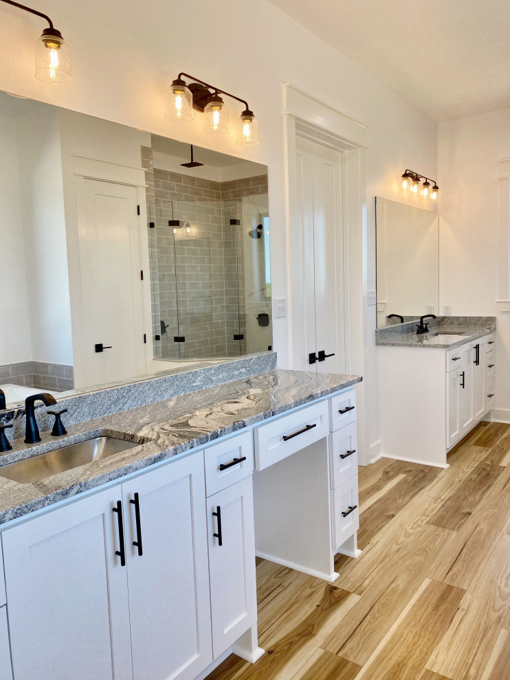 This is an example of a mid-sized country master bathroom in Austin with shaker cabinets, white cabinets, a freestanding tub, a curbless shower, a two-piece toilet, gray tile, subway tile, white walls, laminate floors, an undermount sink, granite benchtops, brown floor, a hinged shower door, black benchtops, a shower seat, a double vanity and a built-in vanity.