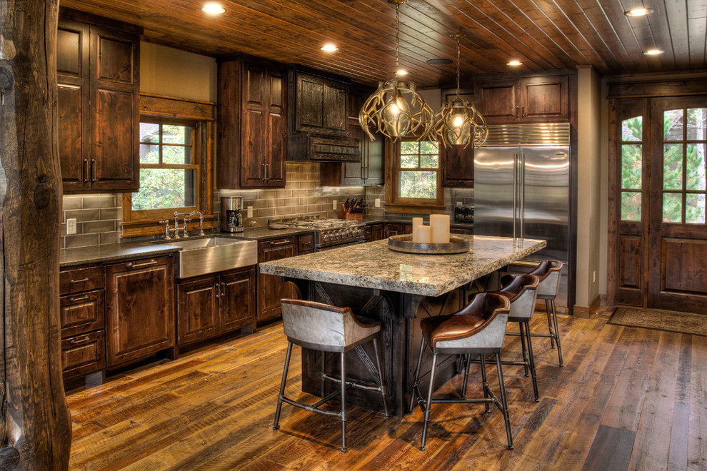 Photo of a country kitchen in Minneapolis with a farmhouse sink, raised-panel cabinets, dark wood cabinets, grey splashback, subway tile splashback, stainless steel appliances, dark hardwood floors, with island and brown floor.