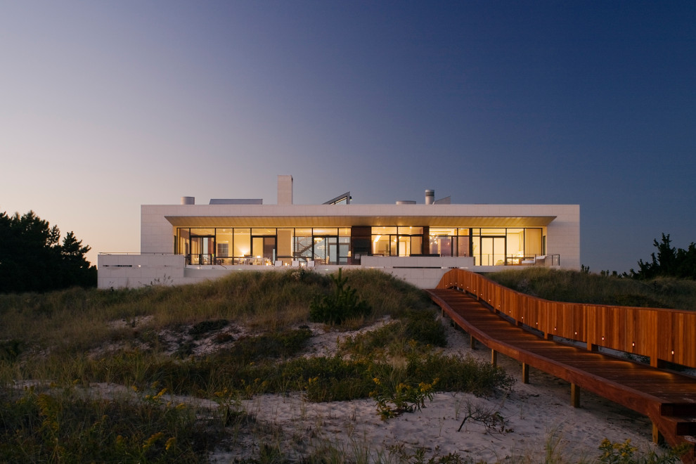 Стильный дизайн: огромный, трехэтажный, белый частный загородный дом в морском стиле с облицовкой из камня и плоской крышей - последний тренд