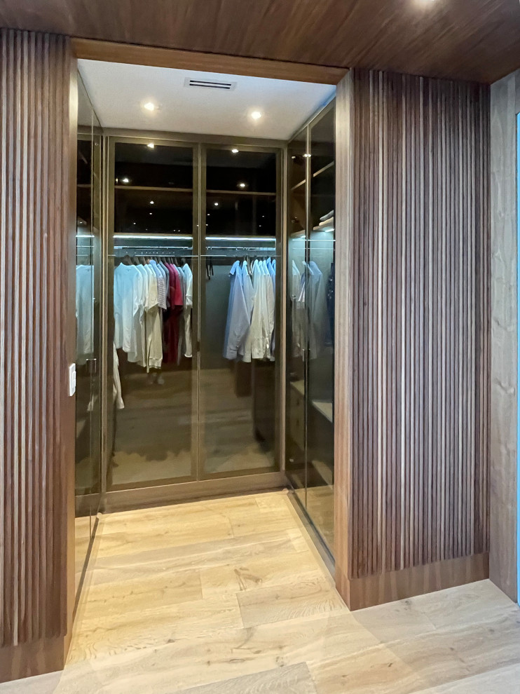 Design ideas for a mid-sized transitional men's dressing room in Miami with glass-front cabinets, medium wood cabinets, medium hardwood floors, beige floor and wood.