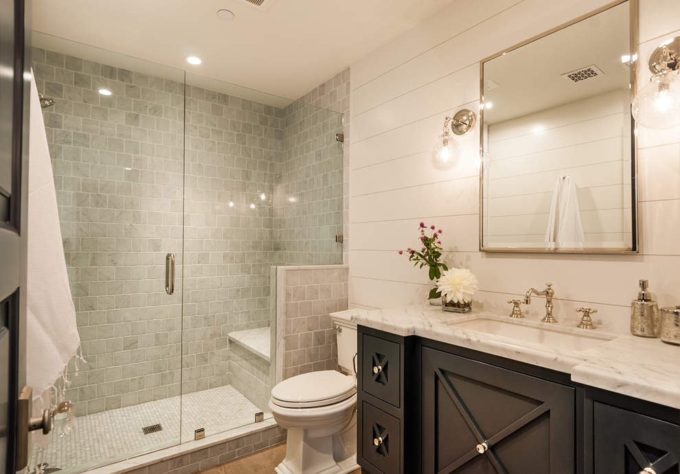 Inspiration for a mid-sized country 3/4 bathroom in Los Angeles with furniture-like cabinets, blue cabinets, an alcove shower, gray tile, marble, white walls, light hardwood floors, an undermount sink, marble benchtops, a hinged shower door and white benchtops.