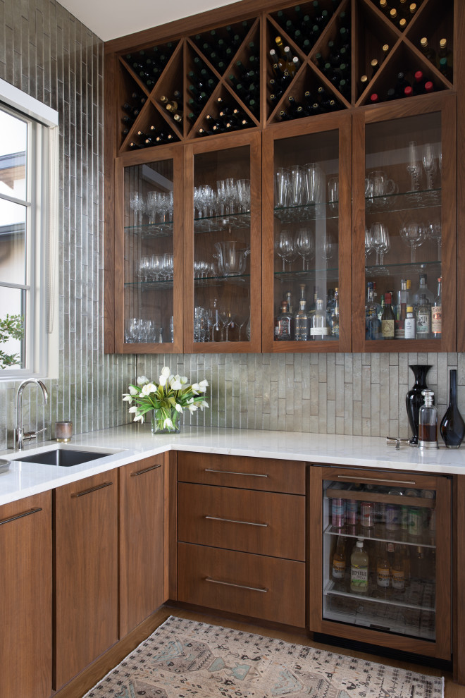 Wet bar - small contemporary l-shaped medium tone wood floor and brown floor wet bar idea in Austin with an undermount sink, medium tone wood cabinets, quartzite countertops, gray backsplash, glass tile backsplash, white countertops and flat-panel cabinets