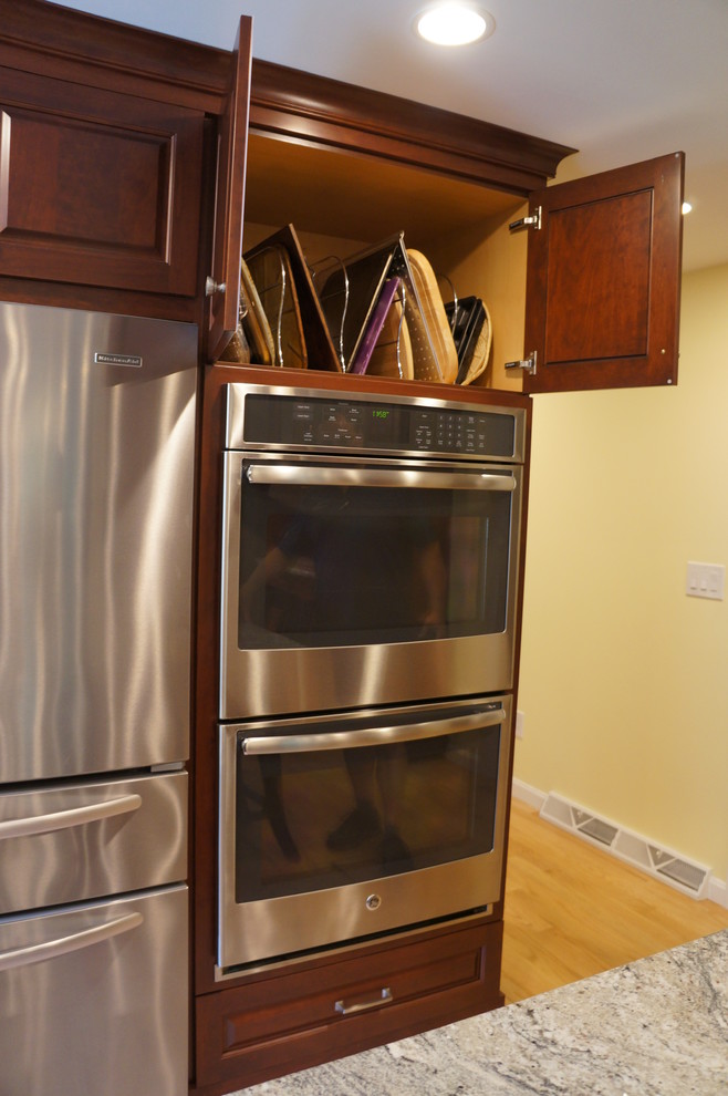 Example of a mid-sized transitional galley light wood floor eat-in kitchen design in Boston with an undermount sink, raised-panel cabinets, dark wood cabinets, quartz countertops, white backsplash, ceramic backsplash, stainless steel appliances and an island