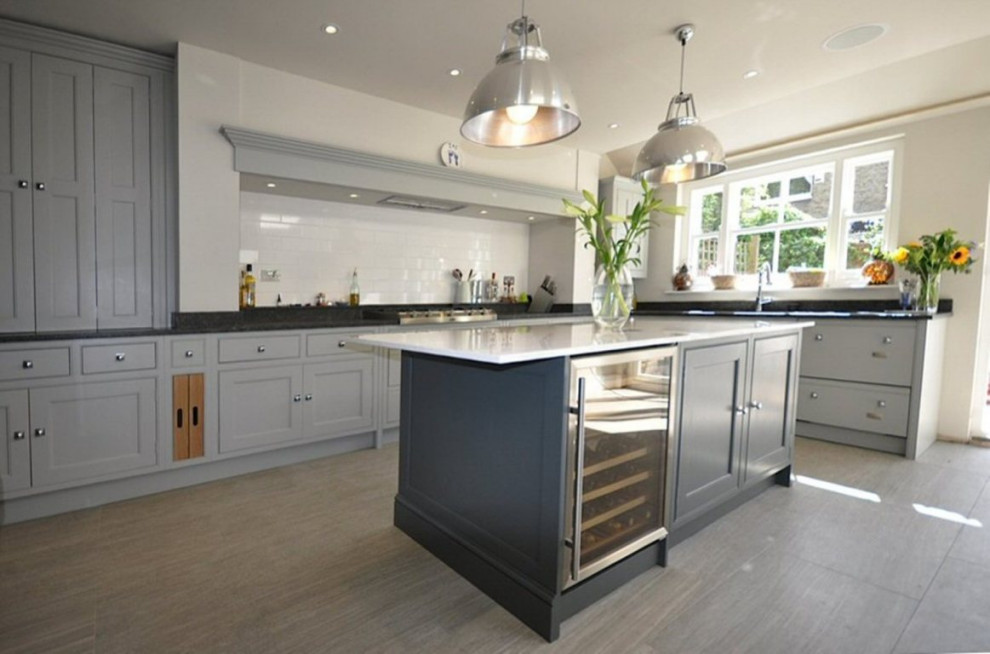 Modern inredning av ett stort grå grått kök, med en undermonterad diskho, luckor med profilerade fronter, grå skåp, granitbänkskiva, vitt stänkskydd, stänkskydd i tunnelbanekakel, integrerade vitvaror, klinkergolv i porslin, en köksö och grått golv