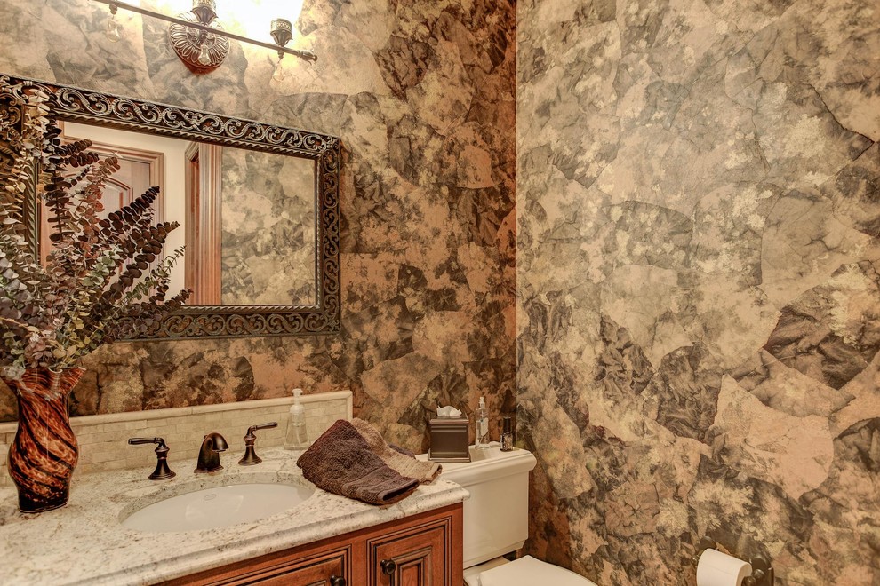 Mid-sized traditional powder room in Denver with raised-panel cabinets, medium wood cabinets, a two-piece toilet, brown walls, an undermount sink, granite benchtops and multi-coloured benchtops.
