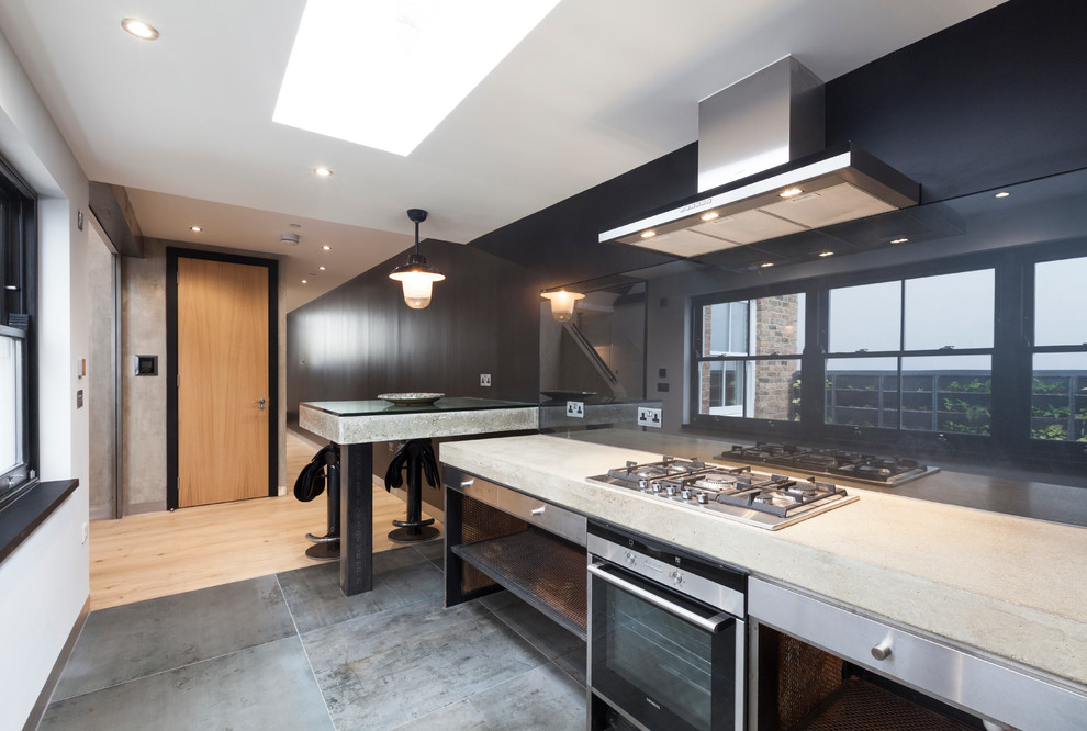Photo of a small contemporary galley separate kitchen in London with a drop-in sink, open cabinets, stainless steel cabinets, concrete benchtops, black splashback, glass sheet splashback, stainless steel appliances, concrete floors and with island.